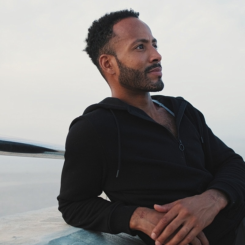 Man in black hoodie gazing thoughtfully outdoors.