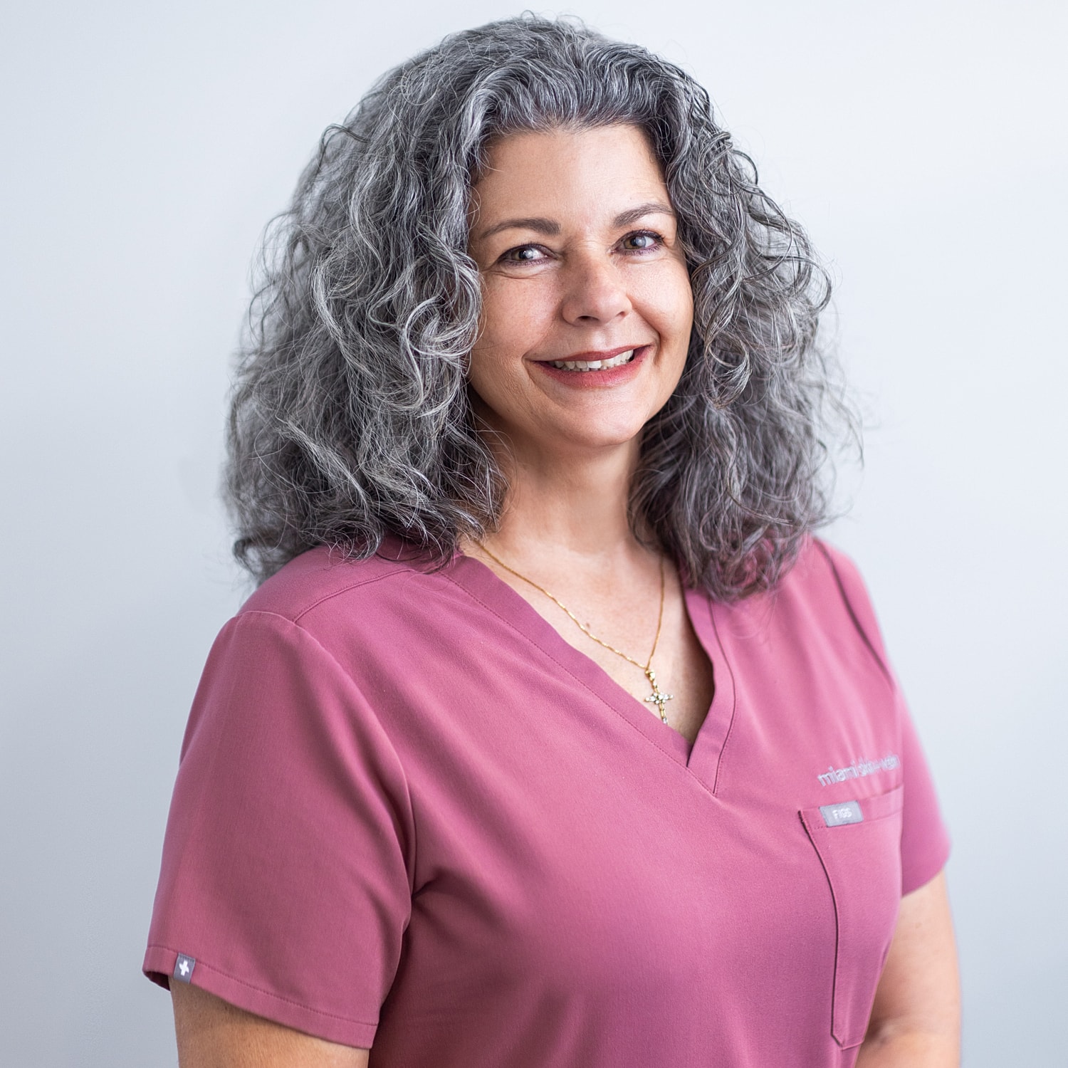 Smiling woman in pink scrubs with curly hair.
