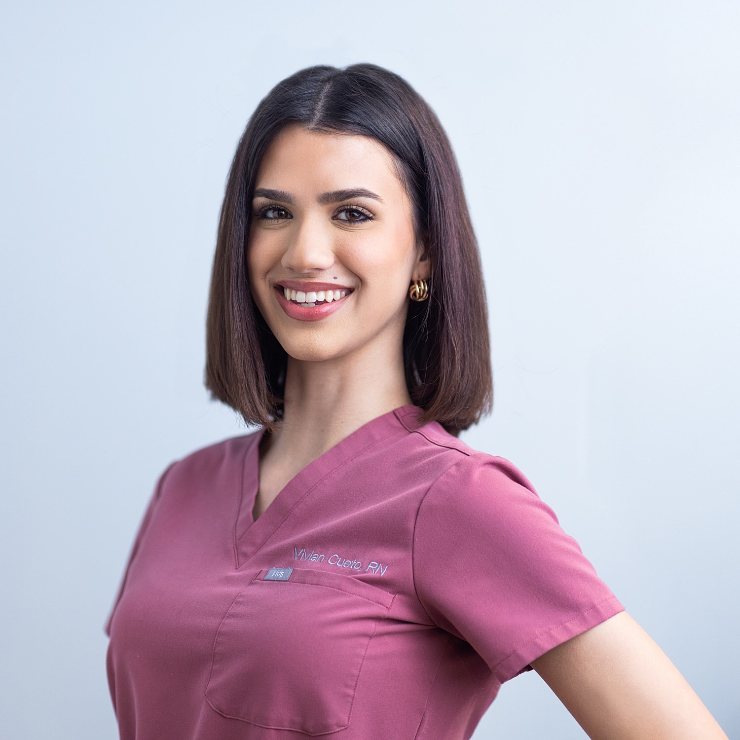 Smiling nurse in pink scrubs against light background.