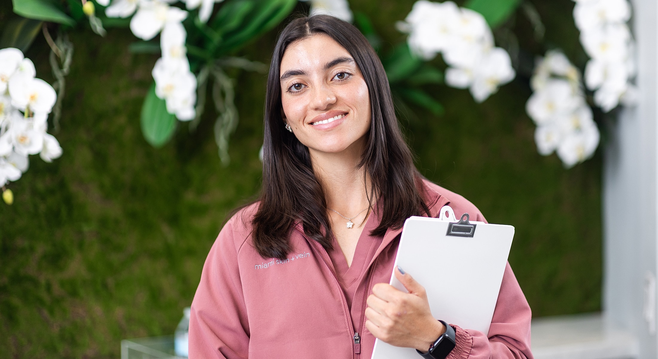 Smiling woman holding clipboard in floral backdrop.