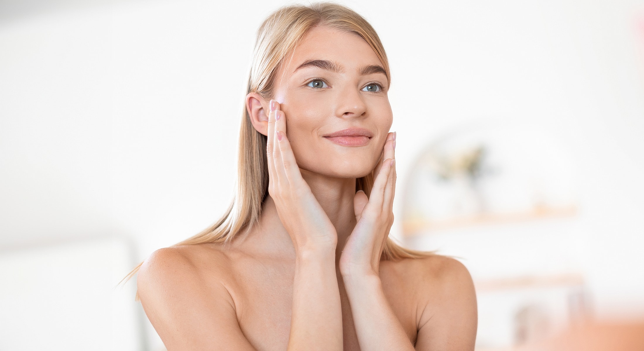 Woman applying skincare, smiling in bright setting.