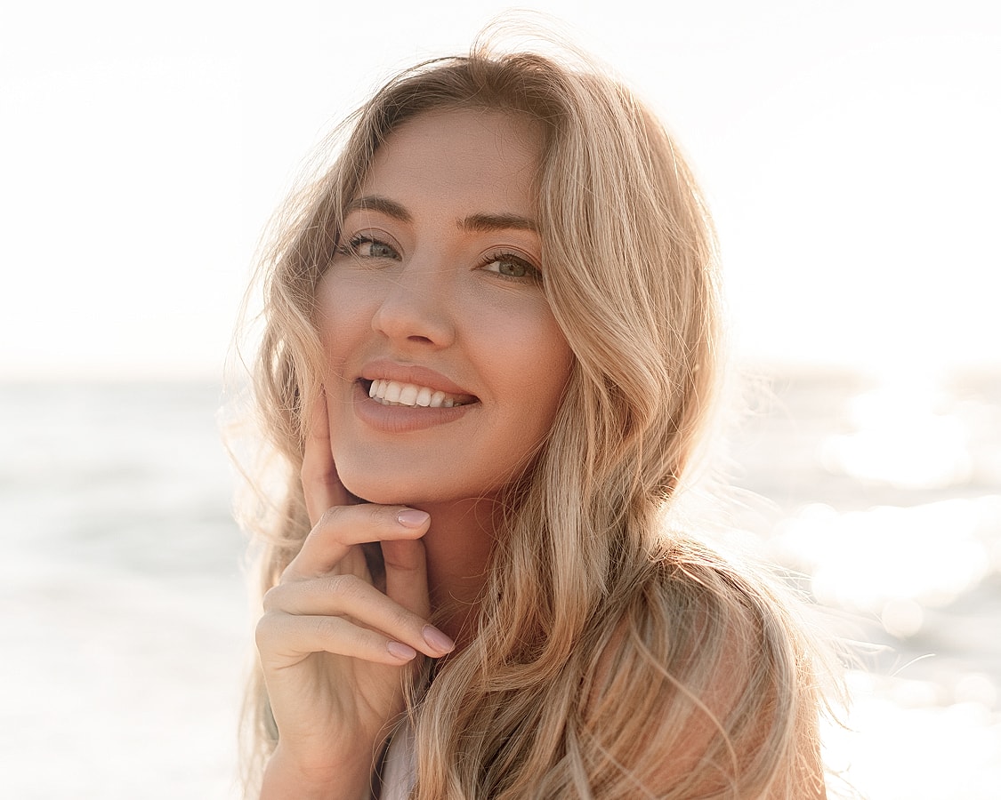 Smiling woman at beach, sunlight background.