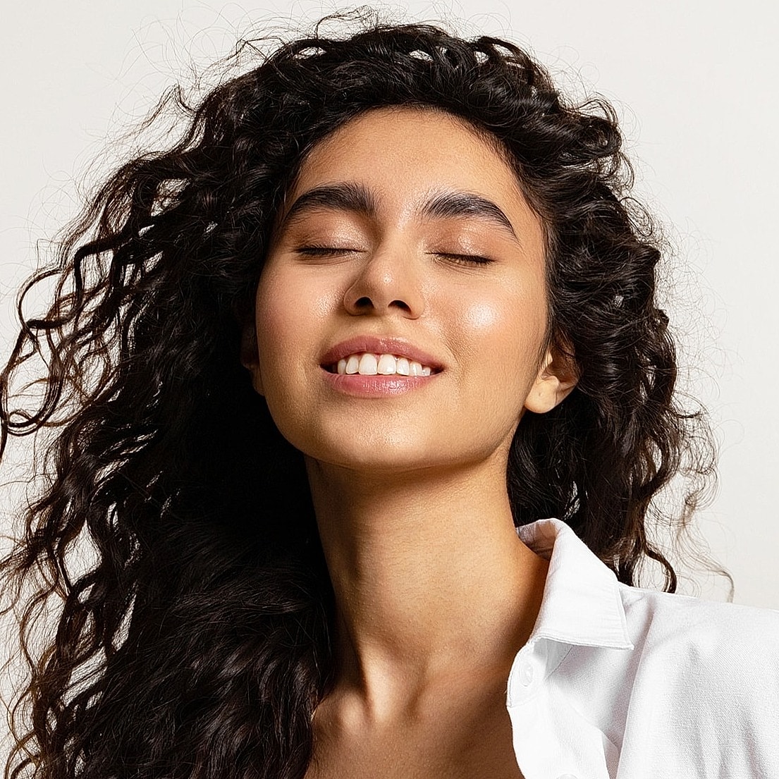 Smiling woman with curly hair and closed eyes.