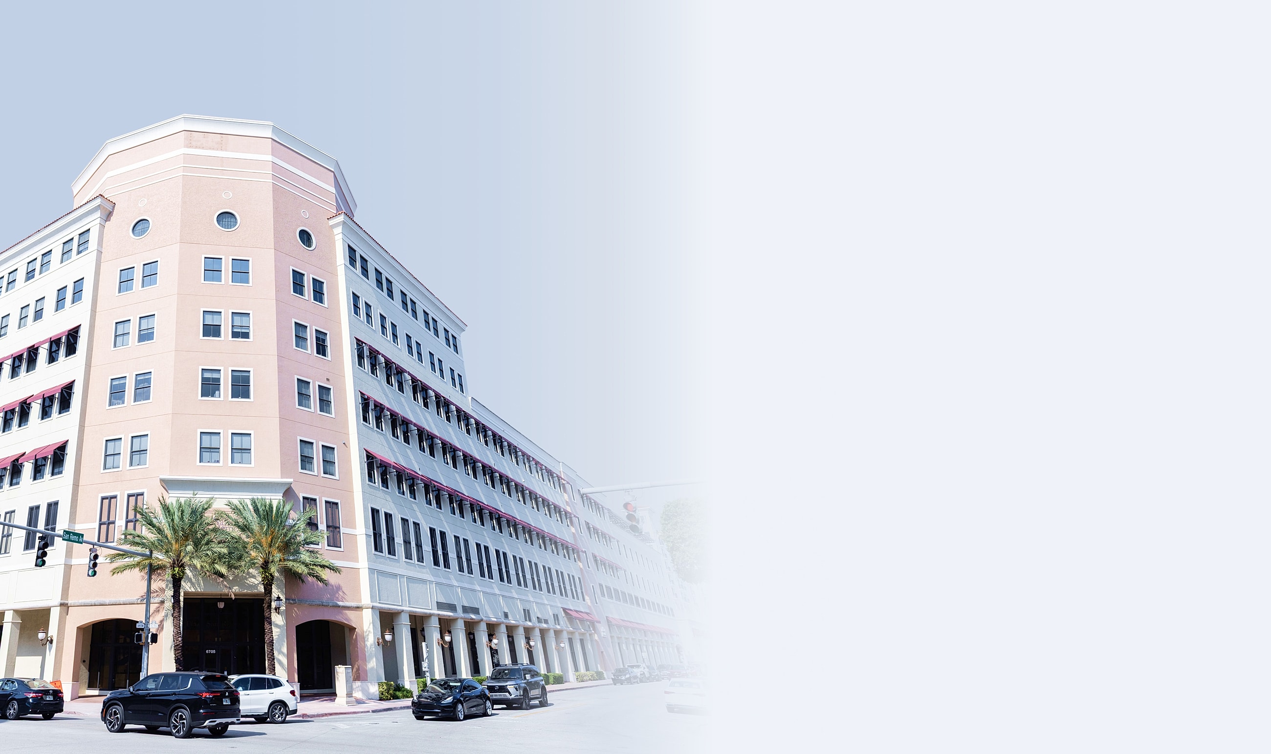 Modern building with palm trees and parked cars.