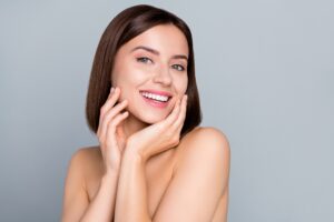 A woman smiling with her hands on her cheeks, showing the results of IPL for redness